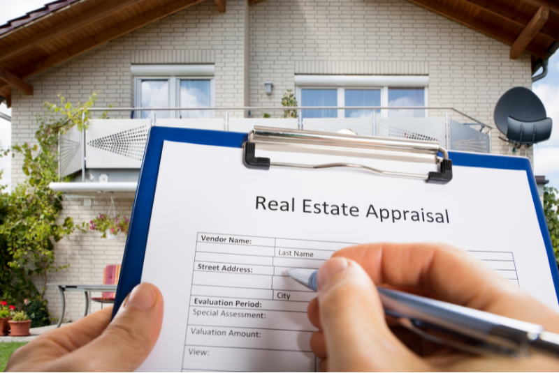 Hands filling out a form on a clipboard titled Real Estate Appraisal.